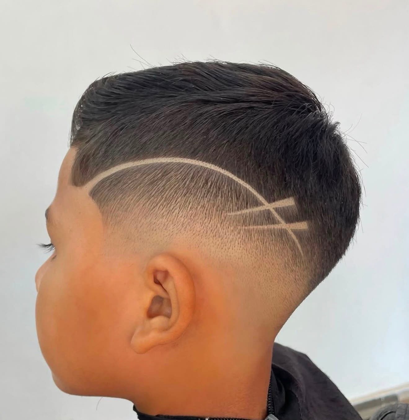 Kinderhaarschnitt im Salon VIP: hoher Fade mit sauber eingeschnittener Linie, seitlich fotografiert