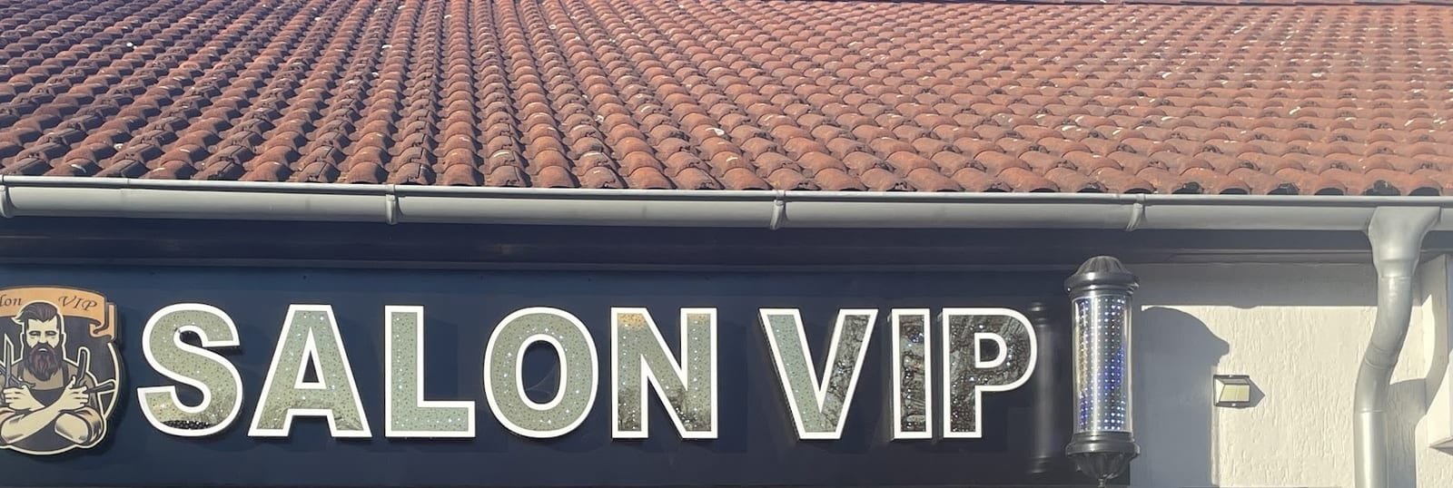 Fassade von Salon VIP mit beleuchtetem Schriftzug, Wappen und Barberstange